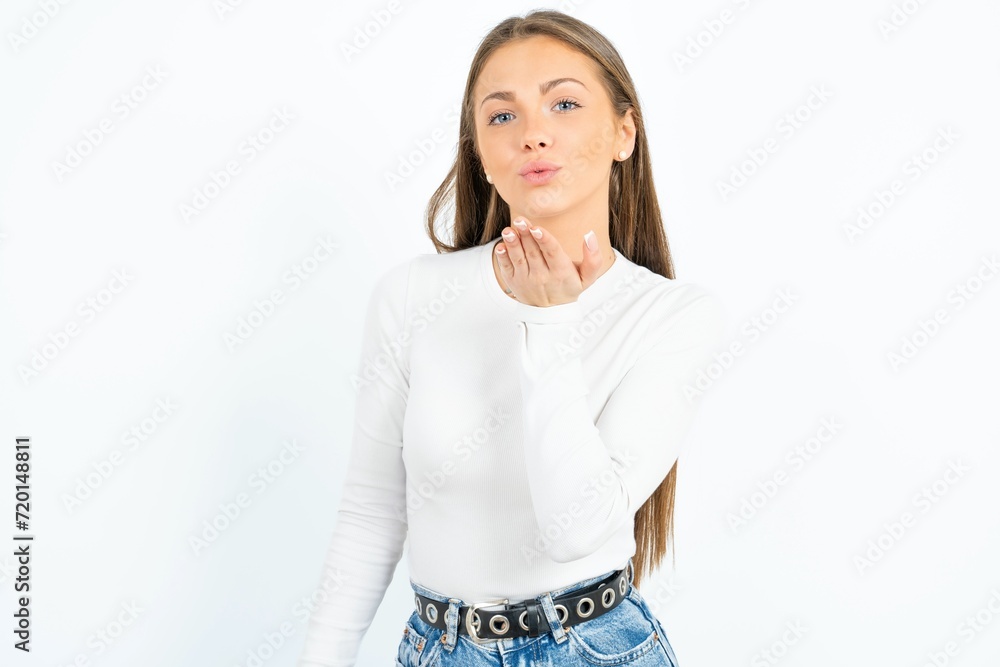 young beautiful girl wearing white T-shirt looking at the camera blowing a kiss with hand on air being lovely and sexy. Love expression. young beautiful girl wearing white T-shirt looking at the camera blowing a kiss with hand on air being lovely and sexy. Love expression.