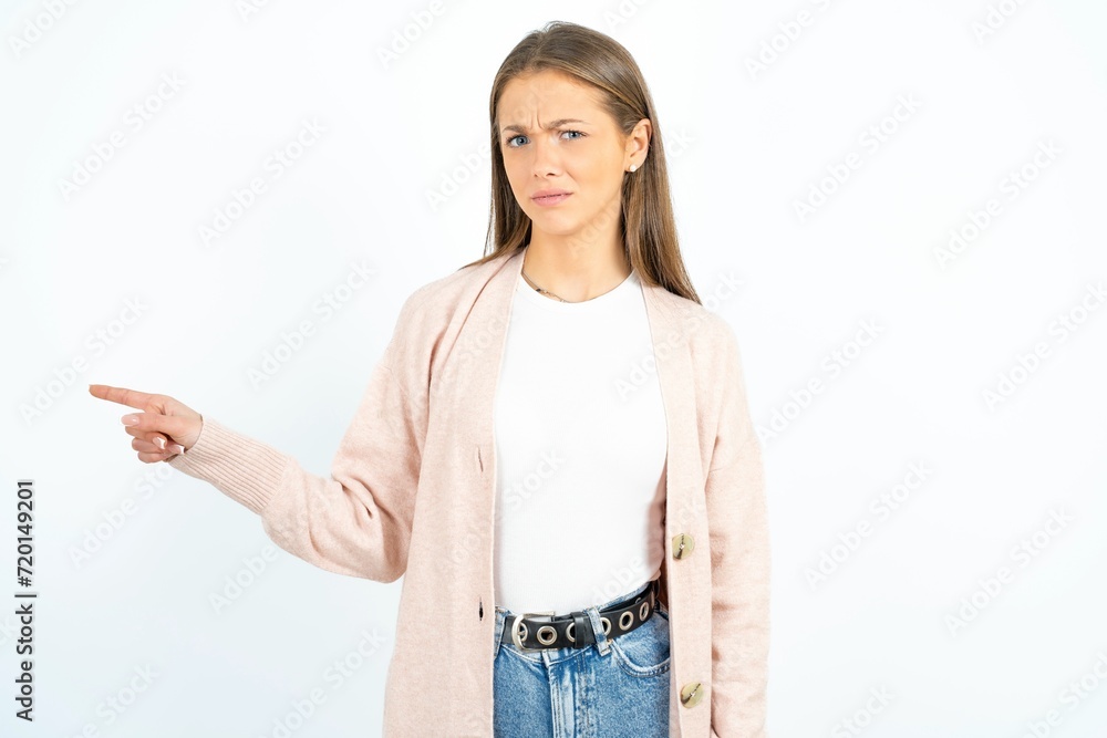 Serious beautiful girl wearing casual clothes smirks face points away on copy space shows something unpleasant. Look at this advertisement. Big price concept Serious beautiful girl wearing casual clothes smirks face points away on copy space shows something unpleasant. Look at this advertisement. Big price concept