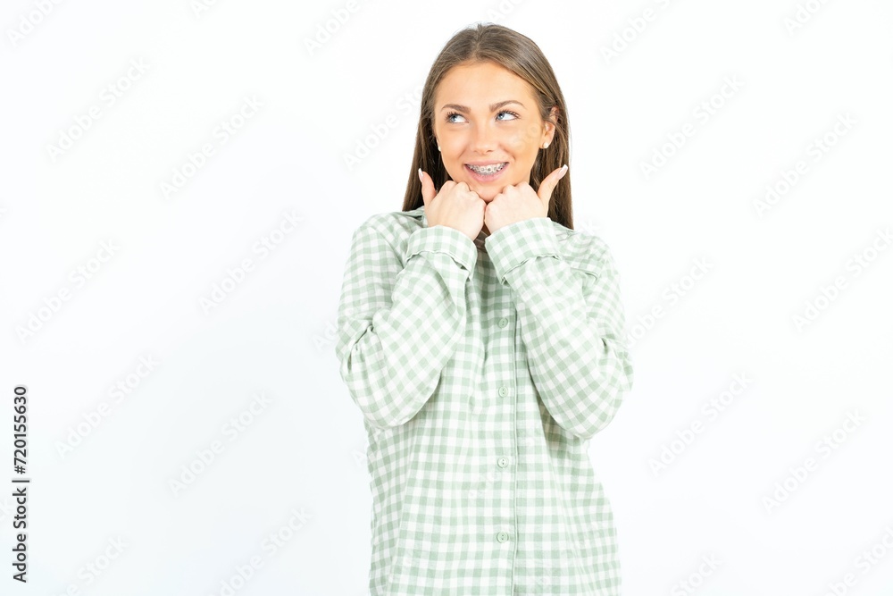 Young beautiful woman standing over white studio background holds hands under chin, glad to hear heartwarming words from stranger Young beautiful woman standing over white studio background holds hands under chin, glad to hear heartwarming words from stranger