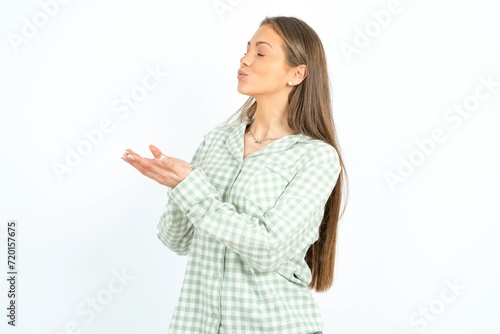 Profile side view, portrait of attractive young beautiful woman wearing green plaid pyjama, sending air kiss