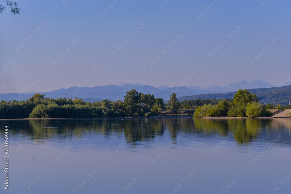 Summer landscape with a blue lake and mountains in the background. Green forest at the edge of the water at the foot of the Carpathians