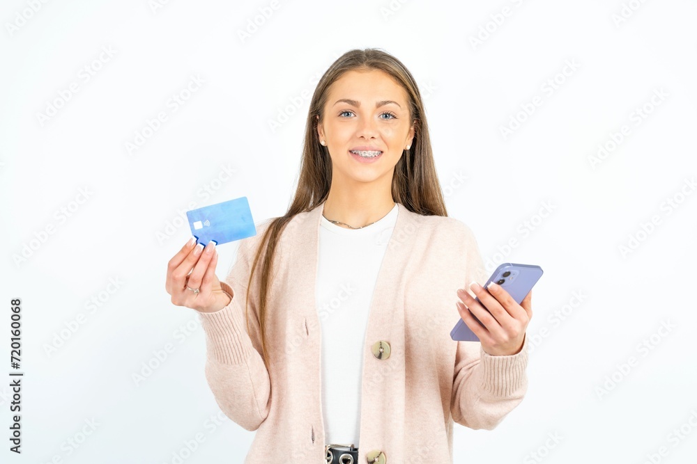 Young beautiful woman wears stereo headphones on ears holds modern mobile phone and credit card Young beautiful woman wears stereo headphones on ears holds modern mobile phone and credit card