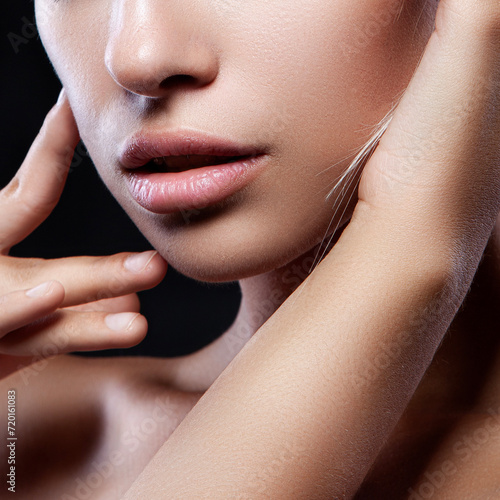 Beauty concept, head and shoulders portrait of beautiful model with nude make-up touching face, closeup. Brunette woman in studio with black background