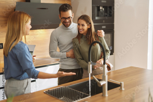 Female shop assistant helping young couple choose new kitchen faucet