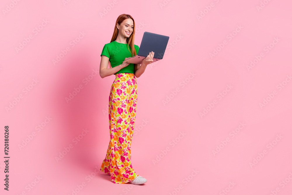 Full size photo of good mood woman with ginger hairdo dressed green t-shirt look at laptop read email isolated on pink color background Full size photo of good mood woman with ginger hairdo dressed green t-shirt look at laptop read email isolated on pink color background
