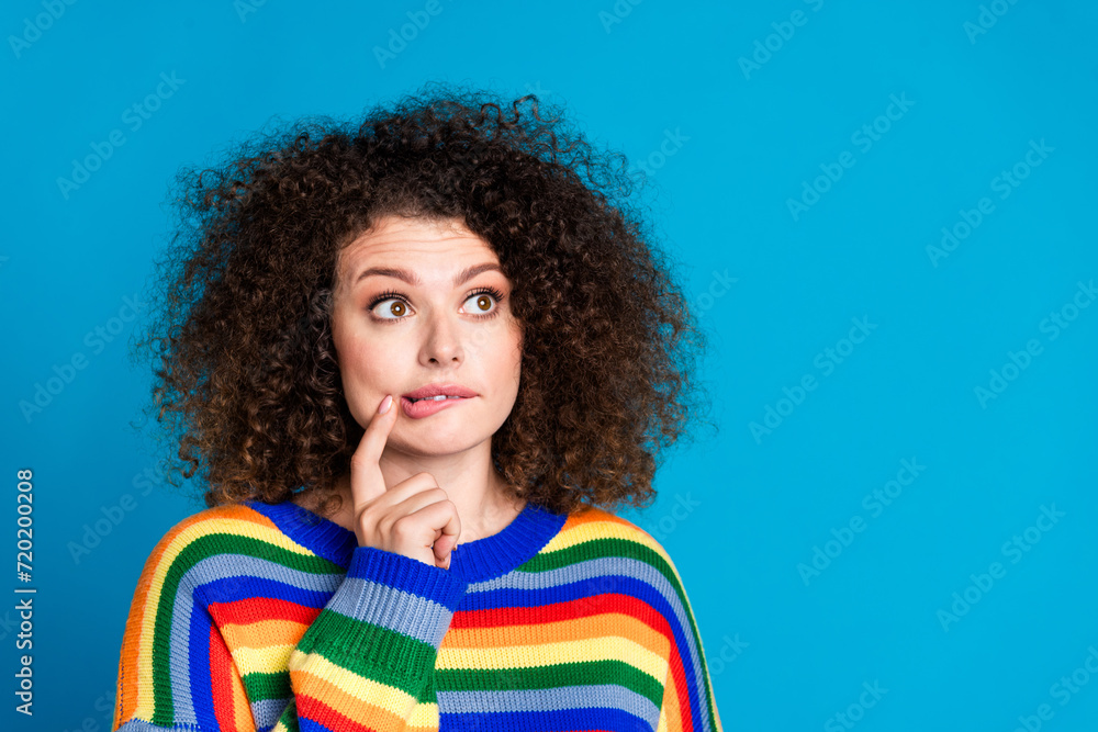 Photo portrait of lovely young lady bite lips look empty space dressed stylish rainbow print garment isolated on blue color background Photo portrait of lovely young lady bite lips look empty space dressed stylish rainbow print garment isolated on blue color background