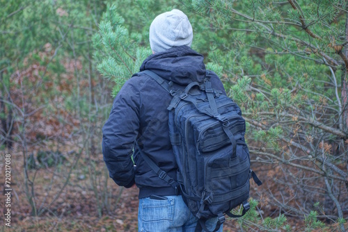 one brack army backpack on the back of a man in a gray hat and jacket on an autumn street