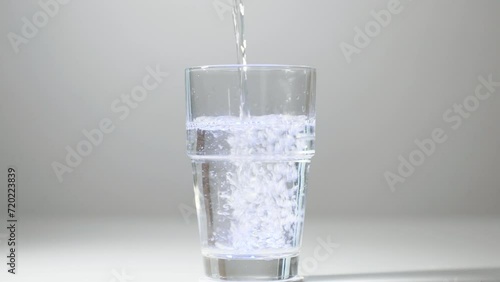 Pouring impure drinking water into a glass with blue light. Close-up of pouring not fresh, contaminated drinking water into a glass on a white background. Drink concept, healthy