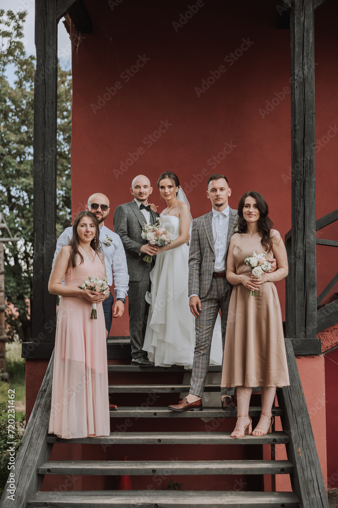 Groom and bride with friends pose on wooden stairs. A beautiful and elegant dress of the bride. Stylish wedding. Summer wedding in nature