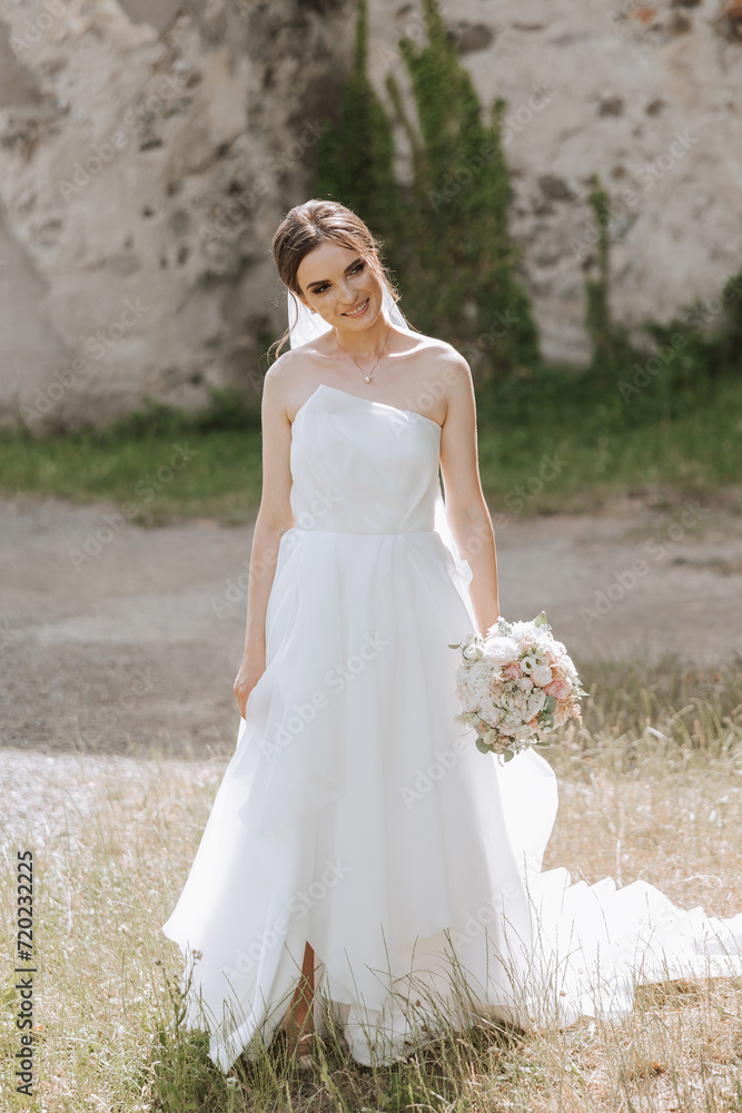 Beautiful bride with a long train. The bride in a white dress with a long train in nature on a summer day. Summer wedding.