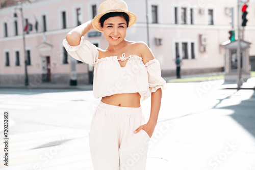 Young beautiful smiling hipster woman in trendy summer costume clothes. Carefree female posing in the street at sunny day. Positive model outdoors at sunset. Cheerful and happy in hat