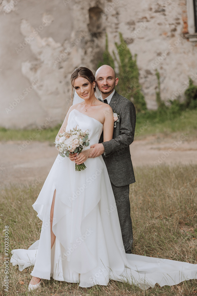A handsome groom embraces his bride in a lush white dress and smiles in a beautiful outdoor setting. Under the open sky. High quality photo. A newlywed couple poses together on a sunny summer day. A handsome groom embraces his bride in a lush white dress and smiles in a beautiful outdoor setting. Under the open sky. High quality photo. A newlywed couple poses together on a sunny summer day.
