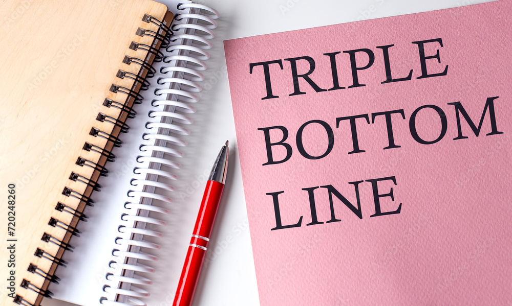 TRIPLE BOTTOM LINE word on the pink paper with office tools on white background TRIPLE BOTTOM LINE word on the pink paper with office tools on white background