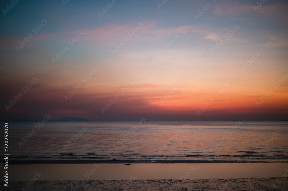 Sky illuminated by the soft hues of a breathtaking sunset or sunrise graces the sea beach, where waves crash rhythmically in the vast ocean. This picturesque scene creates a captivating nature backgro