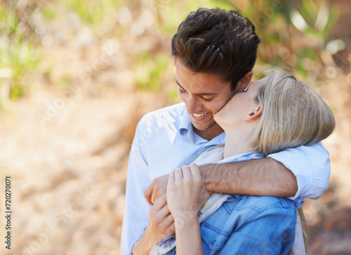 Happy couple, kiss and hug in nature for bonding, love or support in relax for outdoor affection. Face of young woman and man with smile for embrace, comfort or romance in forest or woods together #720270071