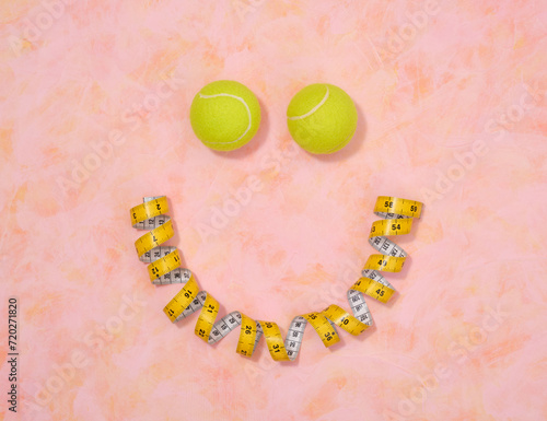 Two yellow tennis balls and a measuring tape in the shape of a smiley face. Fitness and workout wellness concept, top view.