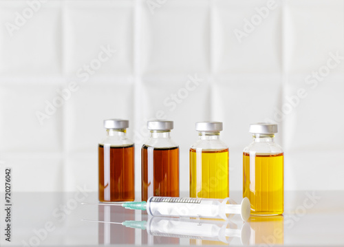 Group of glass bottles of injectable medicine and a syringe on white laboratory table. White background.