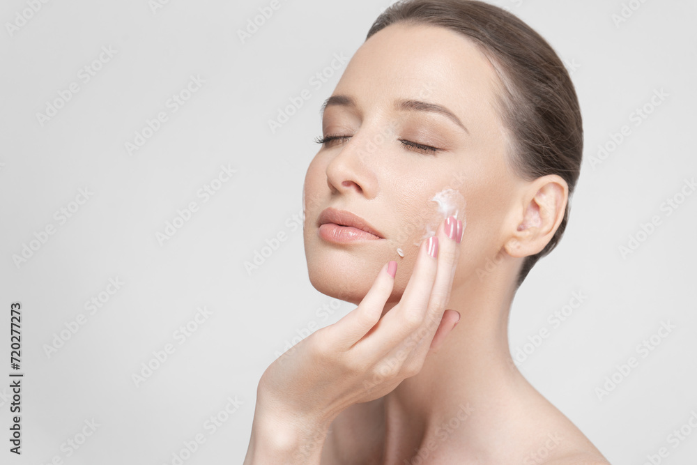 The face of a beautiful girl with clean skin smearing cream on her cheek The face of a beautiful girl with clean skin smearing cream on her cheek