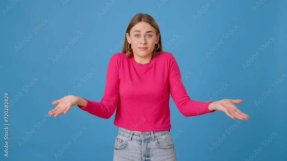 Confused lady spreading hands in bewilderment in blue studio Confused lady spreading hands in bewilderment in blue studio