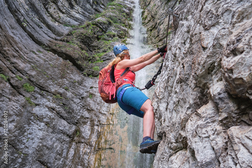 Woman climber on via ferrata next to waterfall, in Italy, Europe. Summer adventure extreme activities.