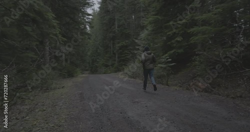 Ungraded 4k wide-angle footage tracking a bearded man wearing bluejeans and a hooded jacket jogging down an unpaved road on an overcast morning at Gifford Pinchot National Forest in Washington State. photo