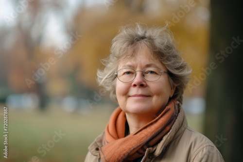 A stylish senior woman with a radiant smile and graceful wrinkles  adorned with glasses and a scarf  poses confidently among autumn trees in this stunning portrait