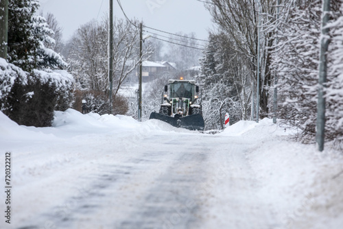 Tractor clears snow on road after heavy snowfall, road maintenance in winter season, harsh weather