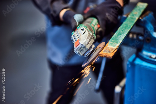 Close-up of a male holding and using a grinder to fix some metal parts, wearing protective gloves. photo