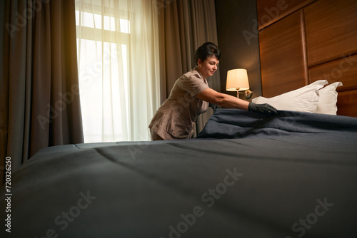 Obraz na plátně Uniformed maid performing in bed-making in guest suite
