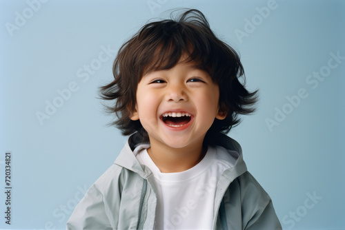 Chinese joyful 4 year old child in simple clothes smiles on a solid color background