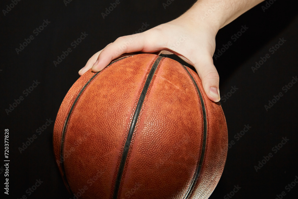 A hand holding a basketball on a dark background in close-up. A hand holding a basketball on a dark background in close-up.