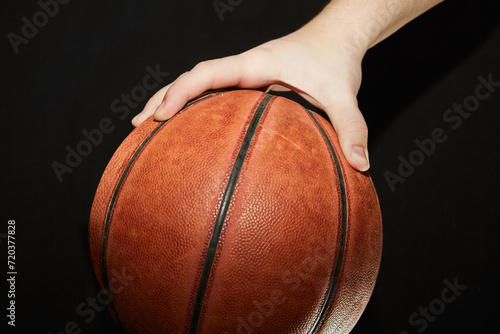 A hand holding a basketball on a dark background in close-up. © Александр Ланевский