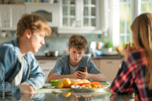 Teenage boy using mobile phone and his arguing parents at table in kitchen