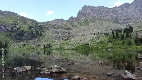 Large stones protruding on a beautiful lake under a fine summer rain in the mountains on a summer day. Marble Lake, Ergaki Nature Park, Krasnoyarsk Territory, Siberia, Russia.