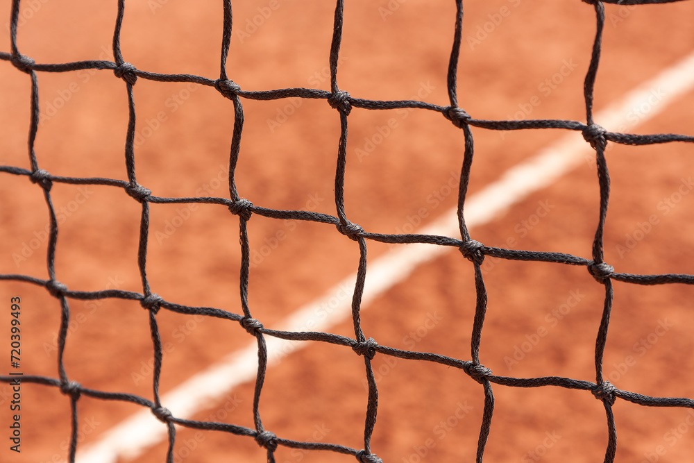Tennis net. Close-up view of the nodes of a sports net against the background of a court with a ground surface Tennis net. Close-up view of the nodes of a sports net against the background of a court with a ground surface