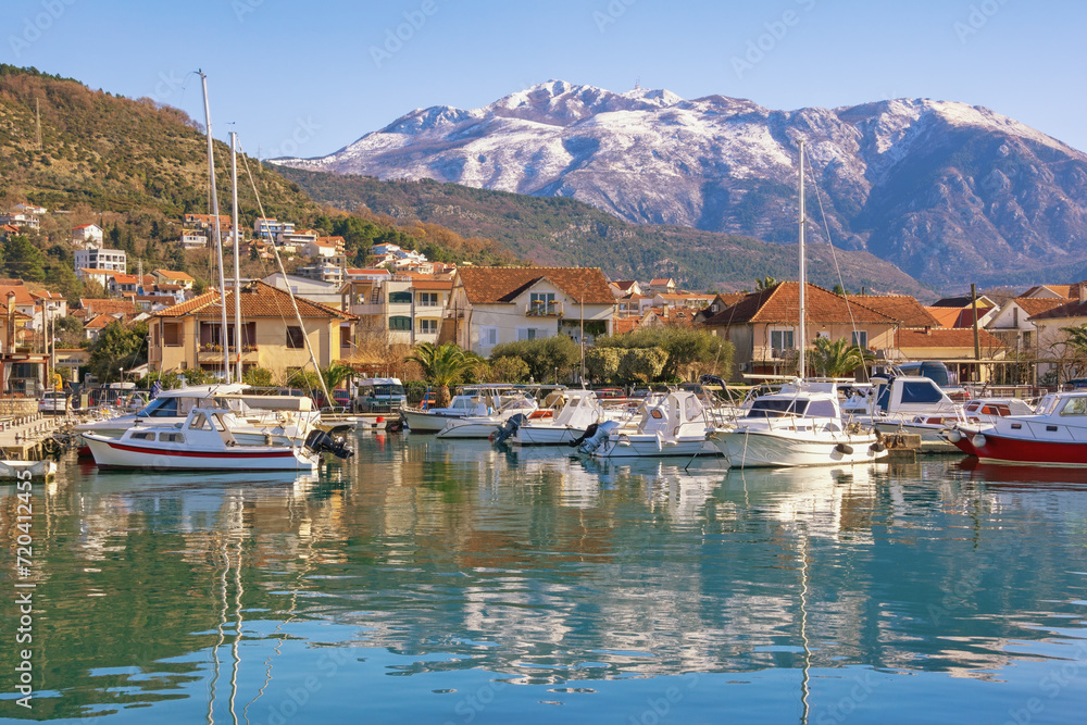 Beautiful winter Mediterranean landscape. Montenegro, Tivat city. Marina Kalimanj and fishing boats in harbor. Snow-capped Lovcen mountains