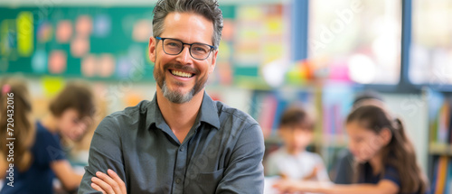 Happy male elementary school teacher. Students are in classroom behind him in a blurry background. Fun and enjoyable learning, love for education concept.