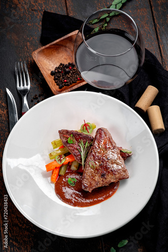Beef liver stewed with demiglas sauce and served with vegetables on a white plate.