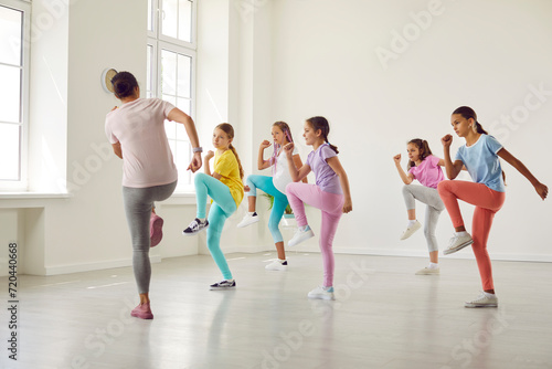 Group of children at dance class. Kids doing sports exercises with professional trainer. Little girl dancers rehearse dynamic moves together with teacher in white room at dance school or youth center
