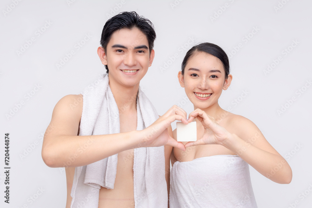 A young asian couple in their early 20s wrapped in white towels poses with a white collagen soap. Making a heart sign together. Isolated on a white backdrop. A young asian couple in their early 20s wrapped in white towels poses with a white collagen soap. Making a heart sign together. Isolated on a white backdrop.