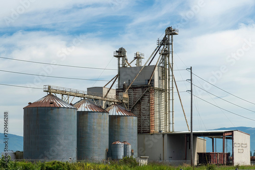 View of a grain crushing facility on a farm in La Conner, WA, USA with mountains in background and blue sky with white feather clouds photo