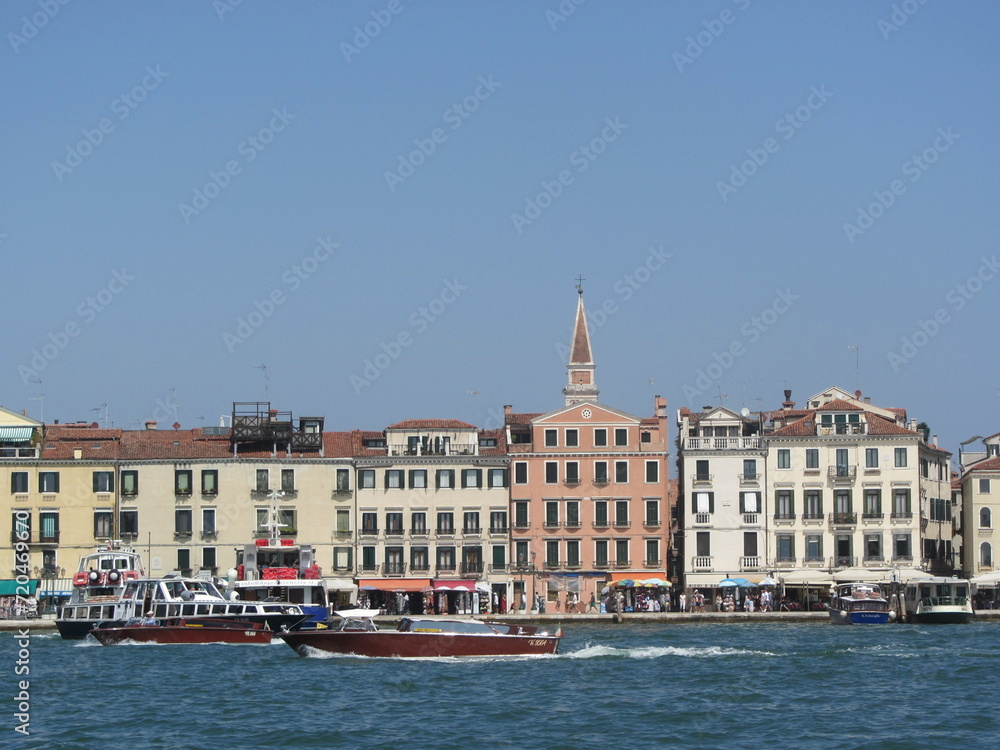 Brown tourist boats sail along the ancient buildings of Venice, leaving behind traces on the water. Waves on the blue sea