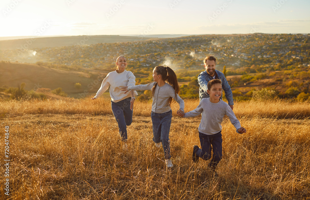 Happy smiling family with two kids daughter and son walking outdoors enjoying beautiful nature. Mother, father with children running outdoors in the field at sunset. Family leisure concept.