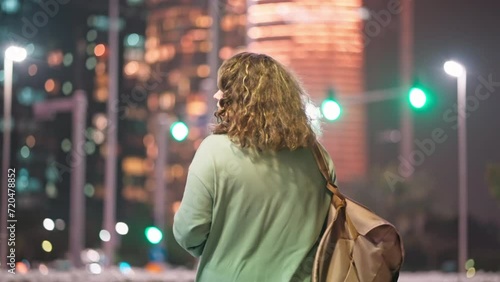 Woman with backpack walking in night city megapolis among skyscrapers in UAE. photo