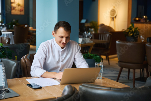 Man in kitchen uniform works with documents in restaurant hall