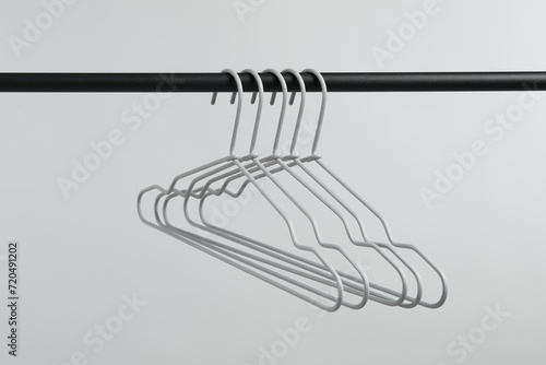 Empty clothes hangers on black rack against light grey background