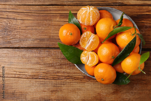 Fresh tangerines with green leaves in bowl on wooden table, top view. Space for text