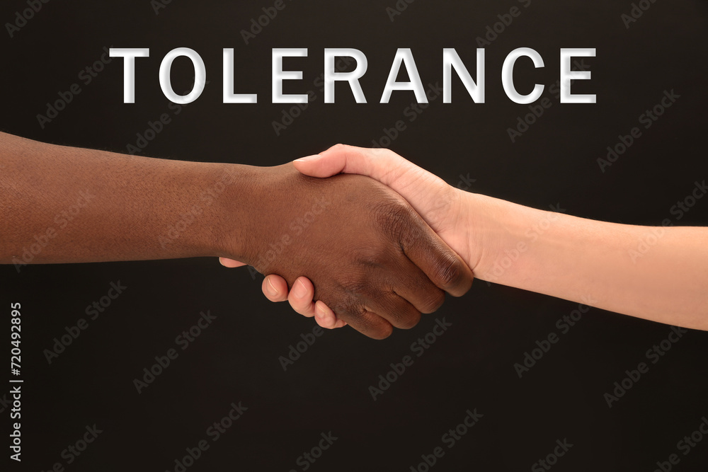 Tolerance, support and cooperation concept. Woman and man of different races shaking hands on black background, closeup Tolerance, support and cooperation concept. Woman and man of different races shaking hands on black background, closeup