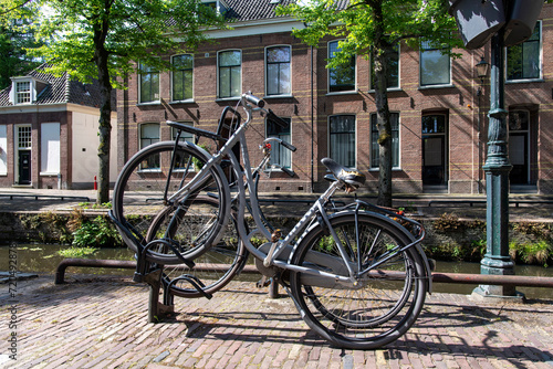 Close up view of two bicycles parked in an angle in a bicycle rack along a typical canal in the Netherlands with canal houses on other side of the water