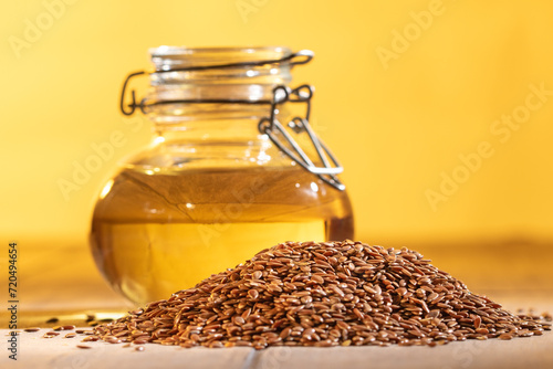 Organic flaxseed oil in glass jar with whole flaxseeds on vibrant orange background